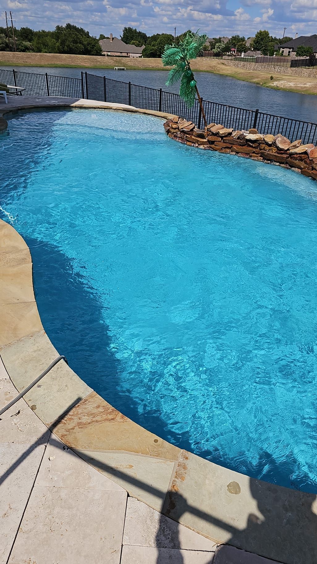 Curved swimming pool with blue water, waterfall feature, and surrounding stone deck.