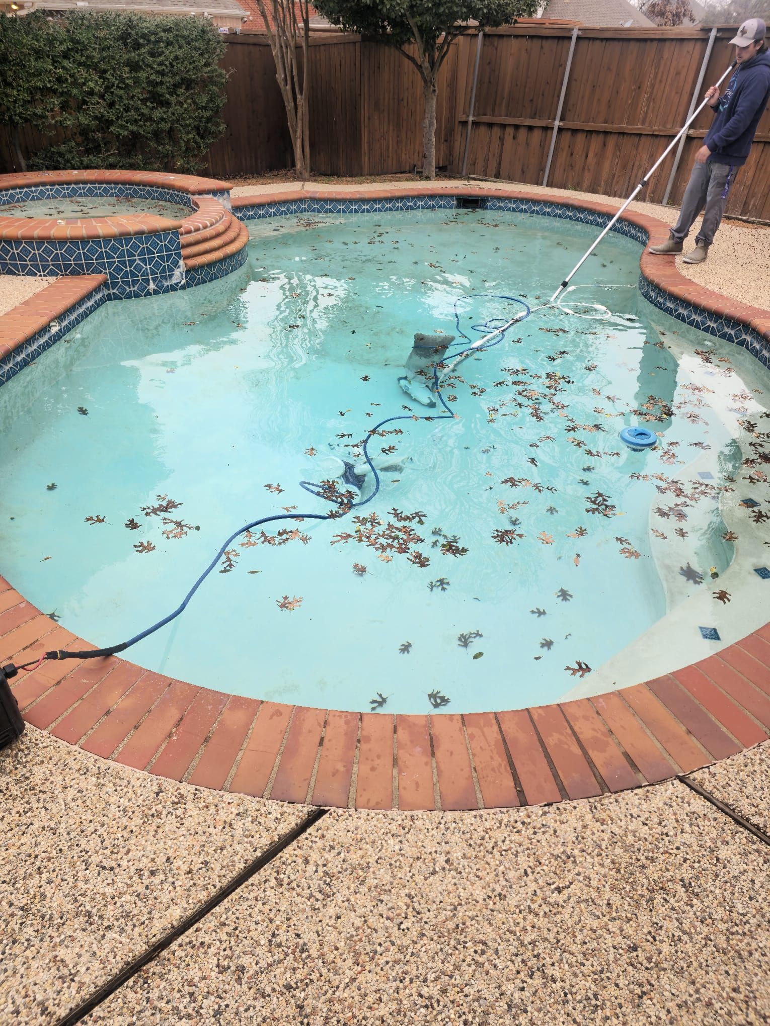 Pool cleaner removing debris from a pool with brick edging and spa.
