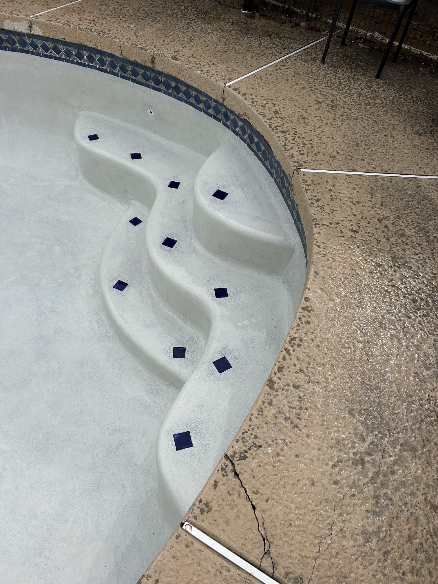 Pool steps with dark blue tile accents. Gray steps curve around the pool's interior.