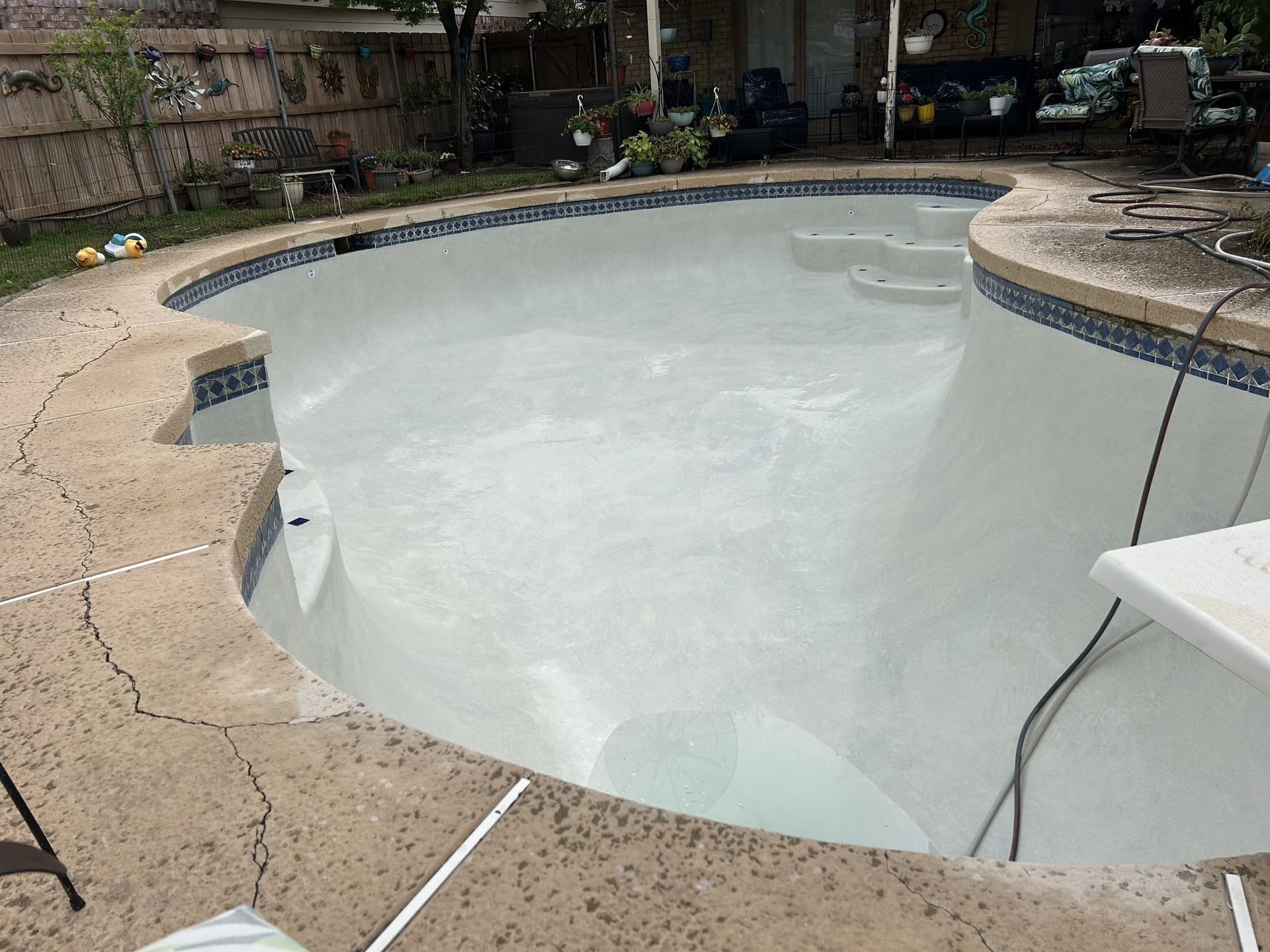 Empty swimming pool with white interior and cracked concrete edging.