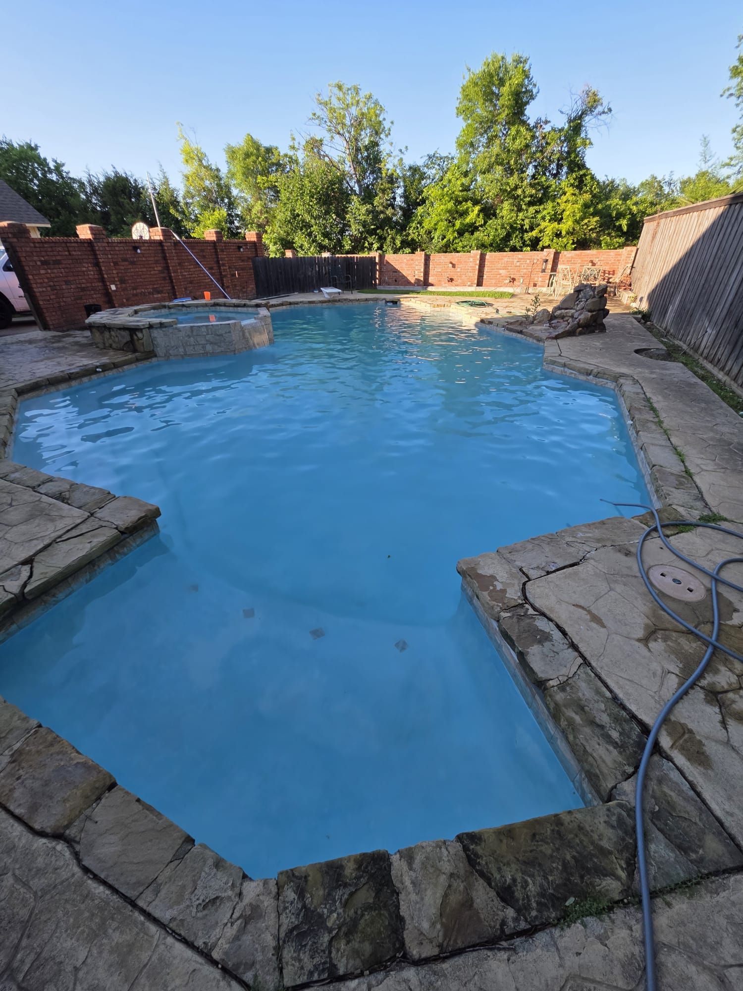 Swimming pool with light blue water surrounded by stone and a brick wall.