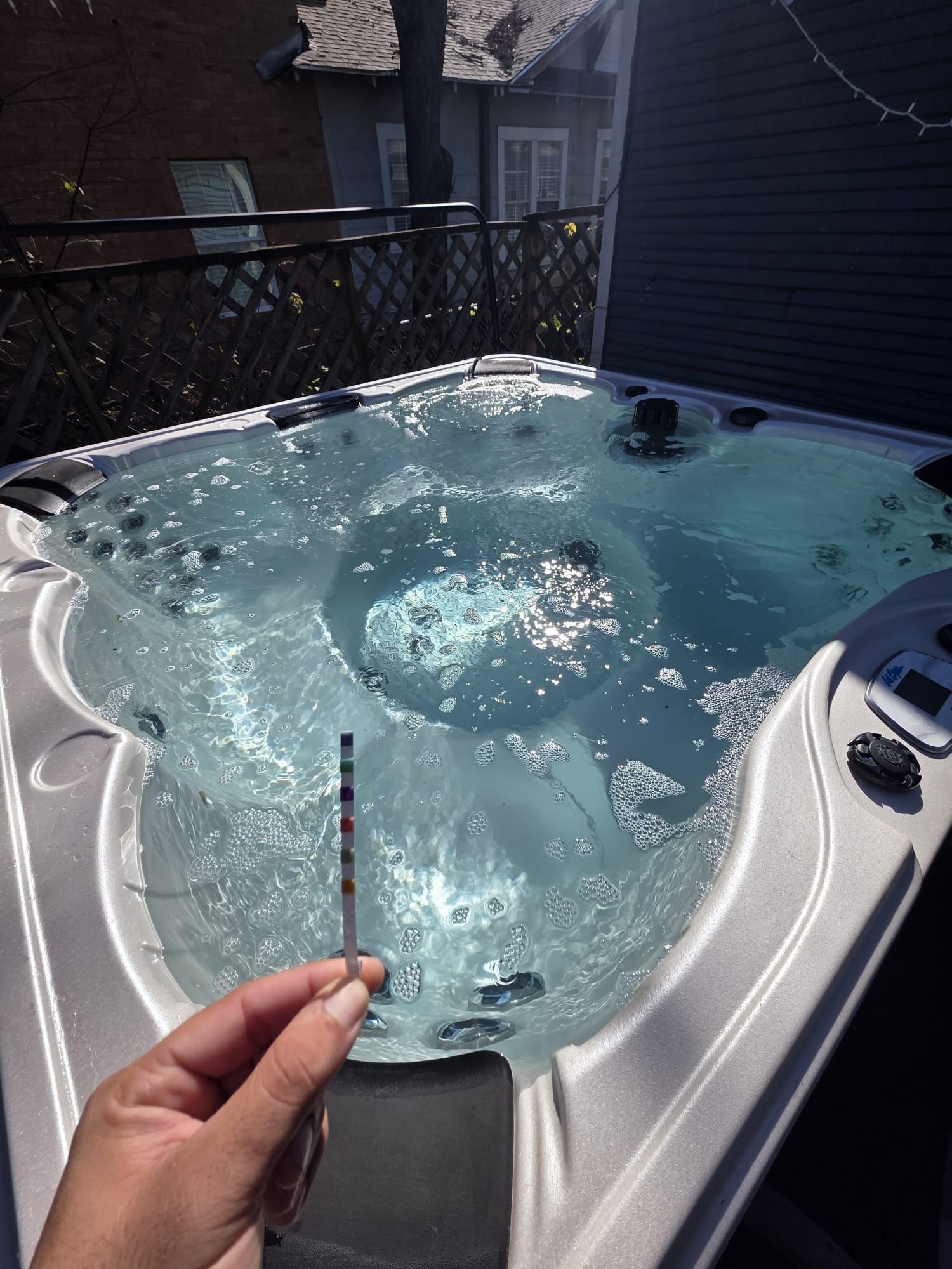 Hand holding a test strip in a bubbling hot tub on a sunny patio.