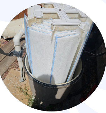 Pool filter cartridge inside a gray bucket, outdoors.
