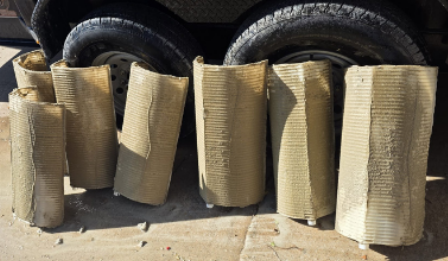 Seven rectangular packages wrapped in beige material, lying on a surface near vehicle tires.