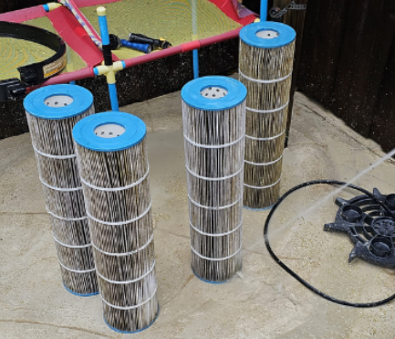 Four cylindrical pool filters with blue tops are being rinsed with water.