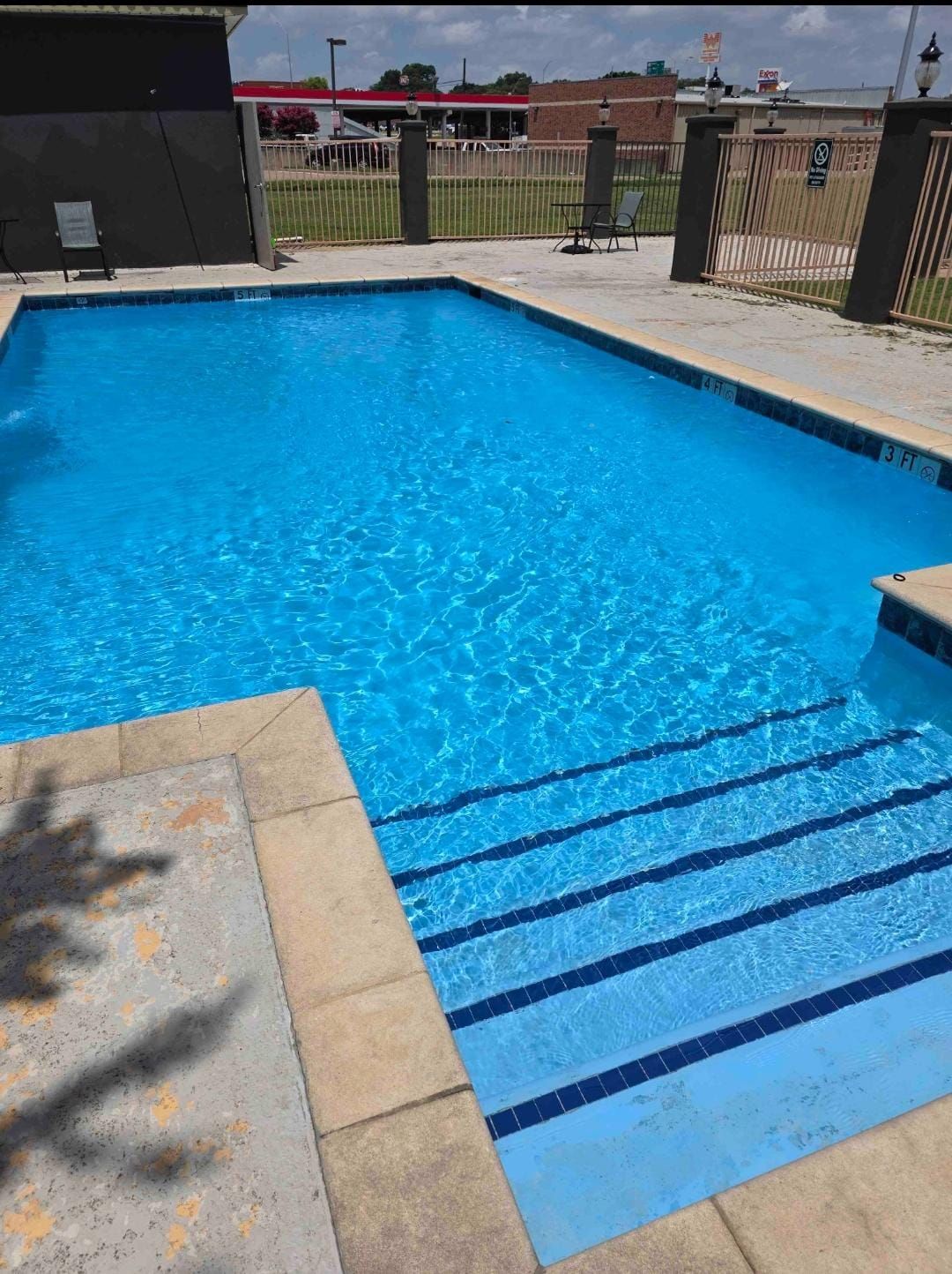 A rectangular swimming pool with clear blue water and steps. Light-colored stone surrounds the pool's edge.