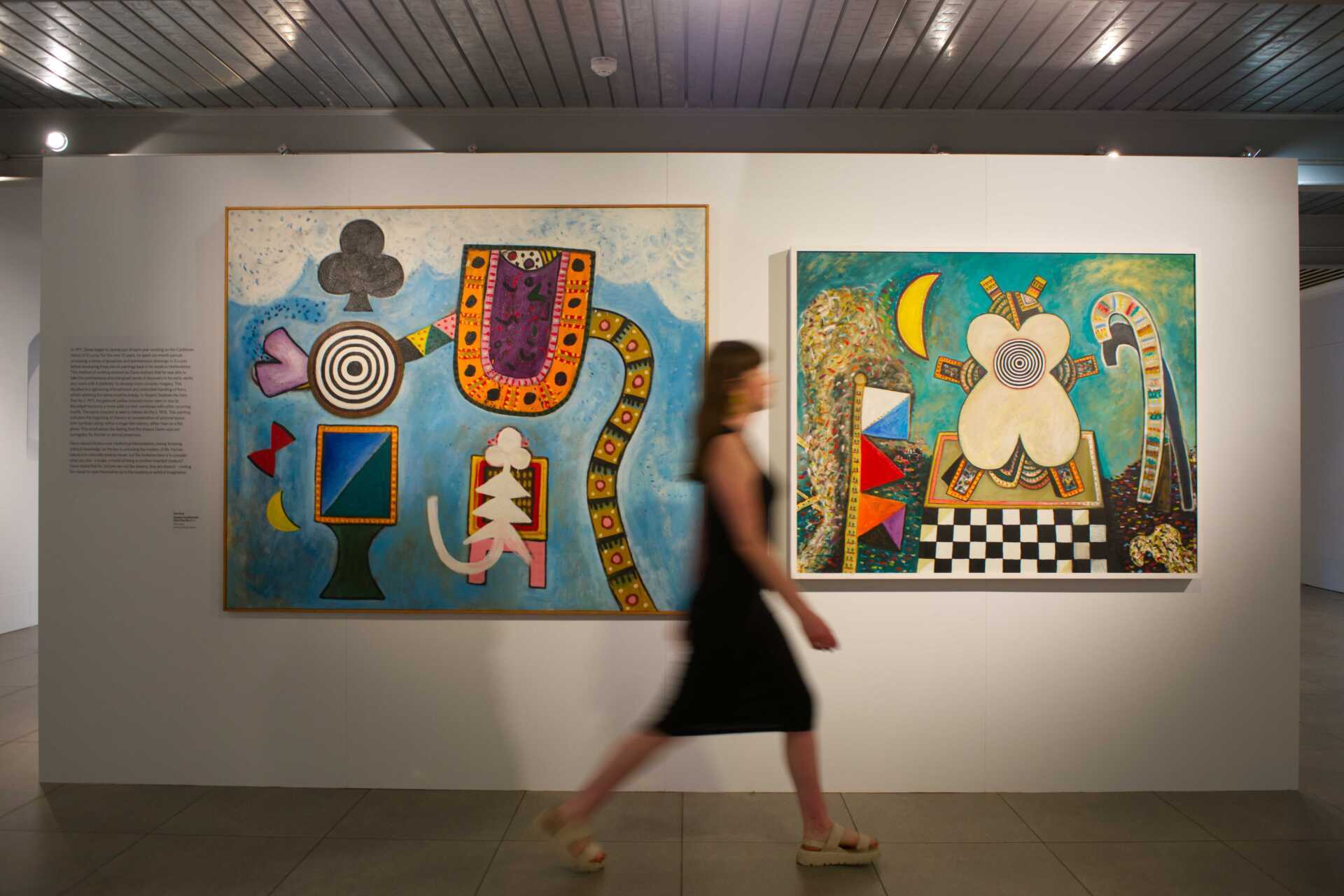 Woman walking across room in front of white wall with two Alan Davie paintings hanging