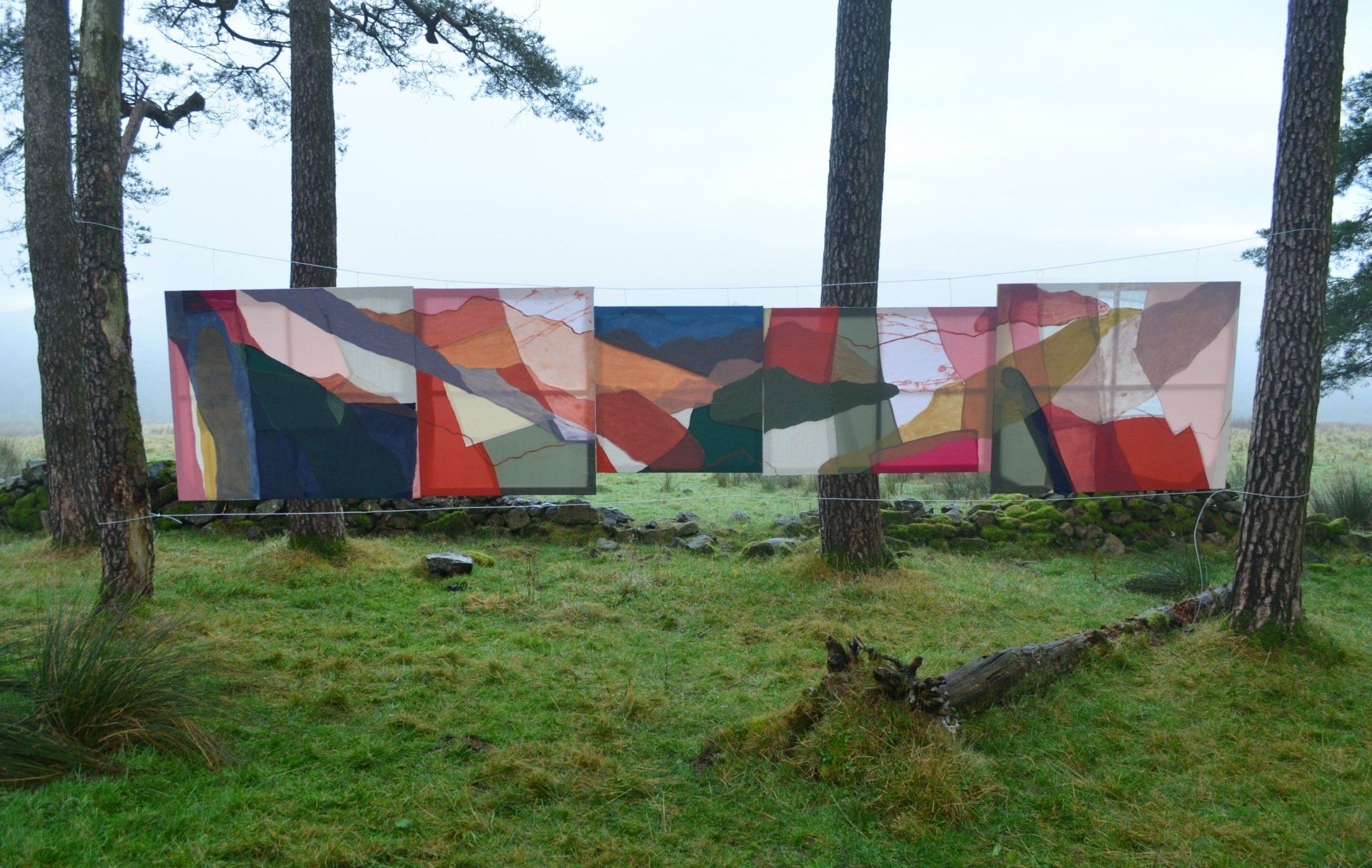 Colourful abstract paintings hung between trees outdoors