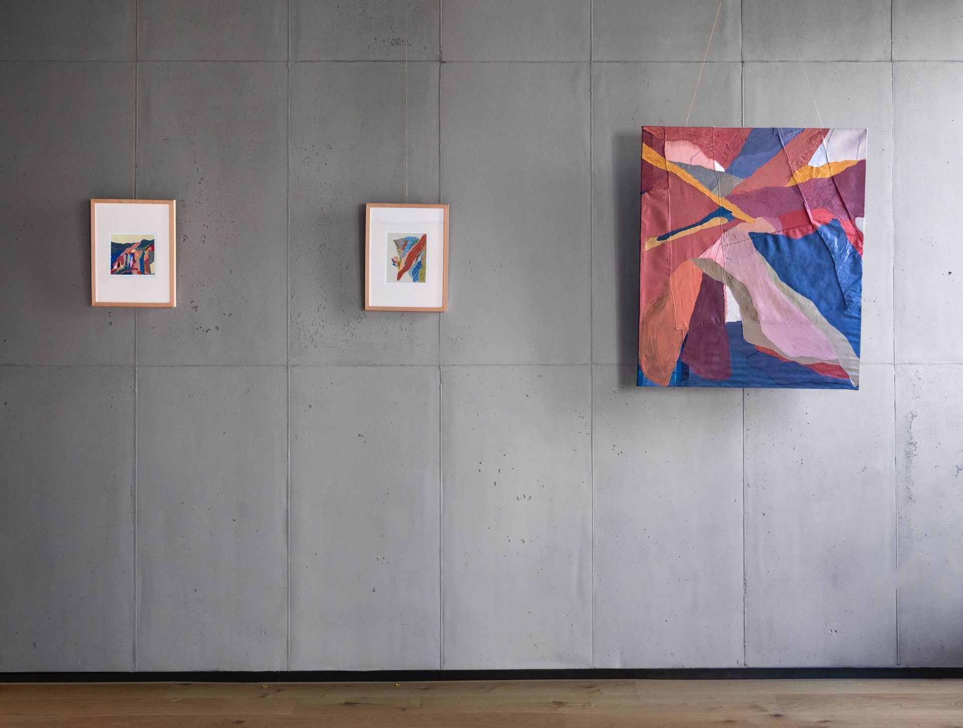 Installation view of colourful paintings on a grey wall 