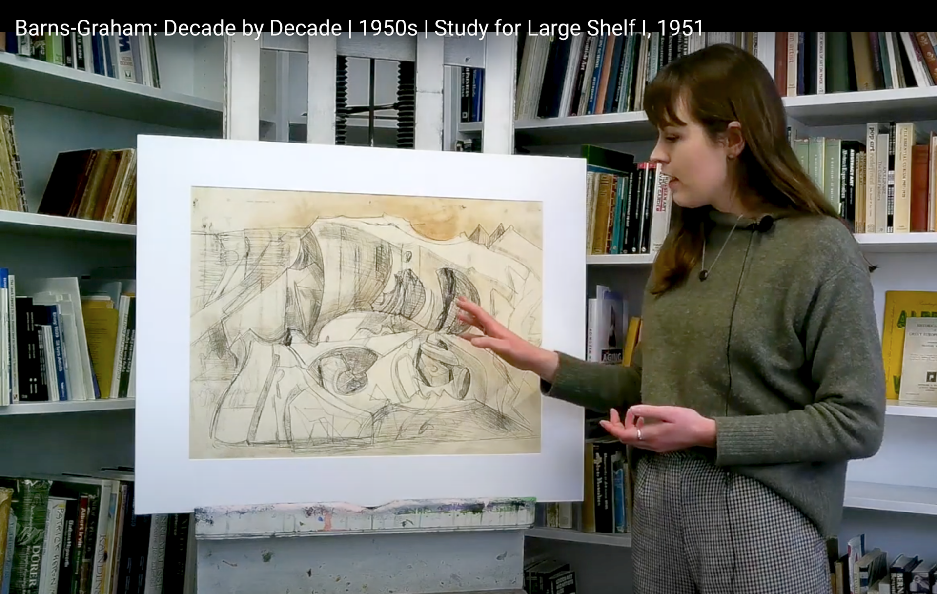 Artist  standing next to drawing, pointing, in a library
