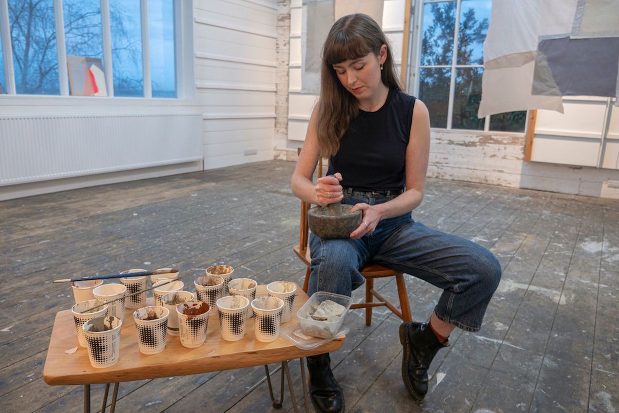 Artist Siobhan McLaughlin sitting in large studio grinding stones into paint