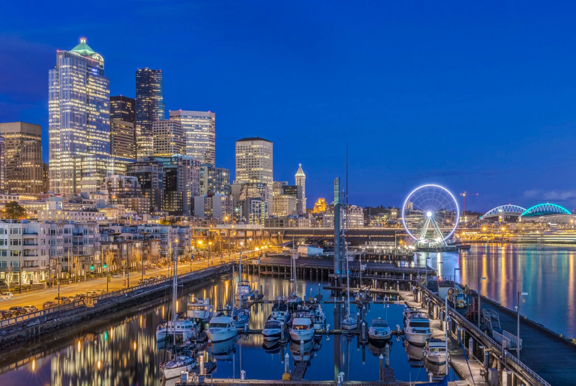 A marina with boats docked in front of a city skyline at night.