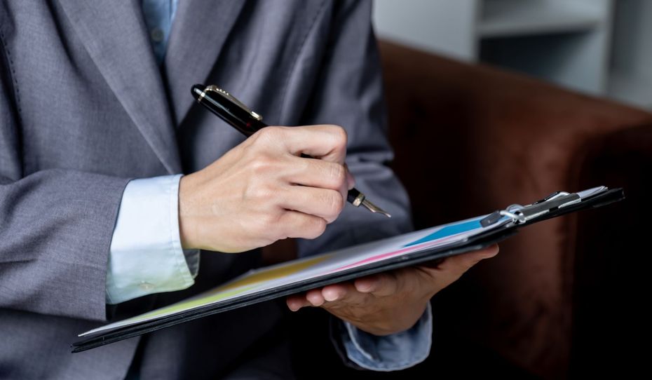A man in a suit is writing on a clipboard with a pen.