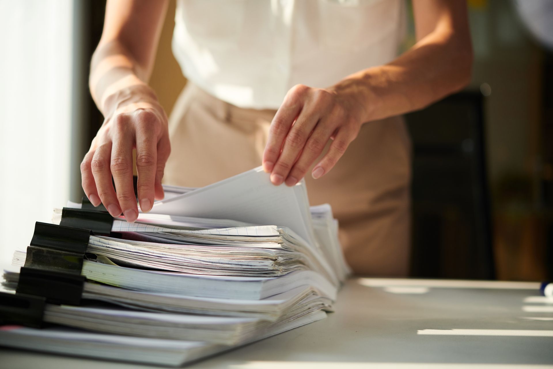 A woman is stacking papers on top of each other on a desk.