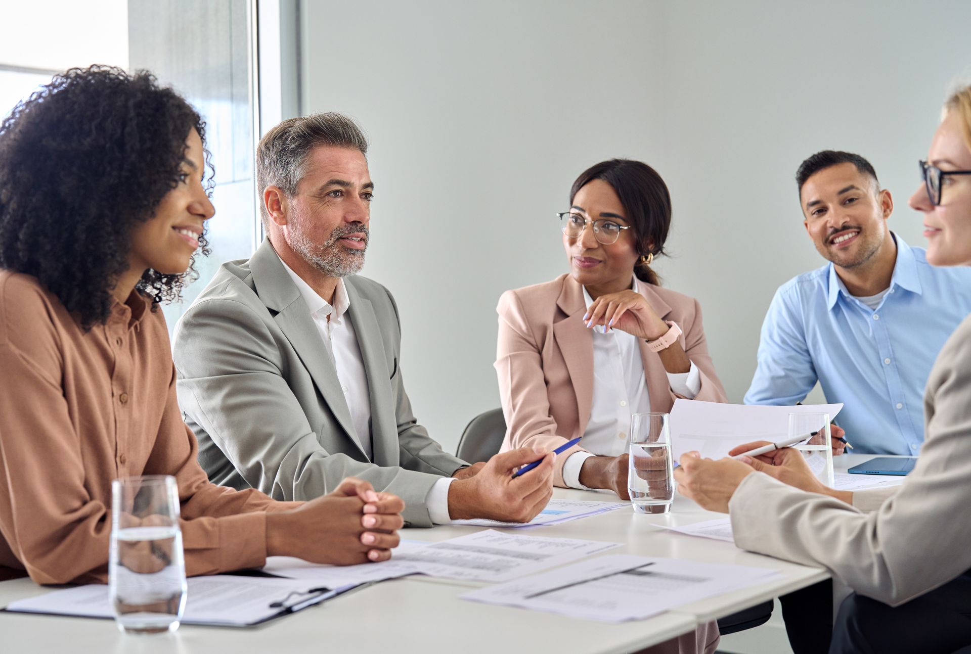 Business colleagues at a table, discussing documents. Smiling faces, modern office setting.