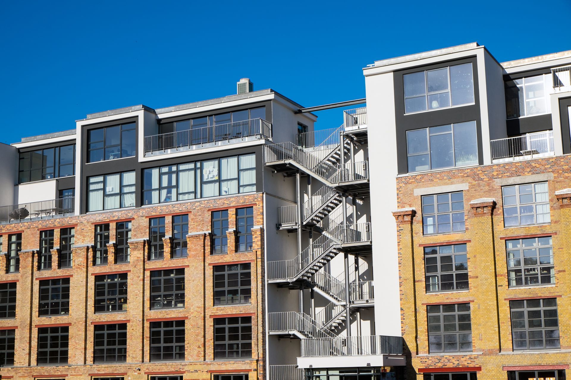 Brick and modern buildings with metal fire escape against a blue sky.