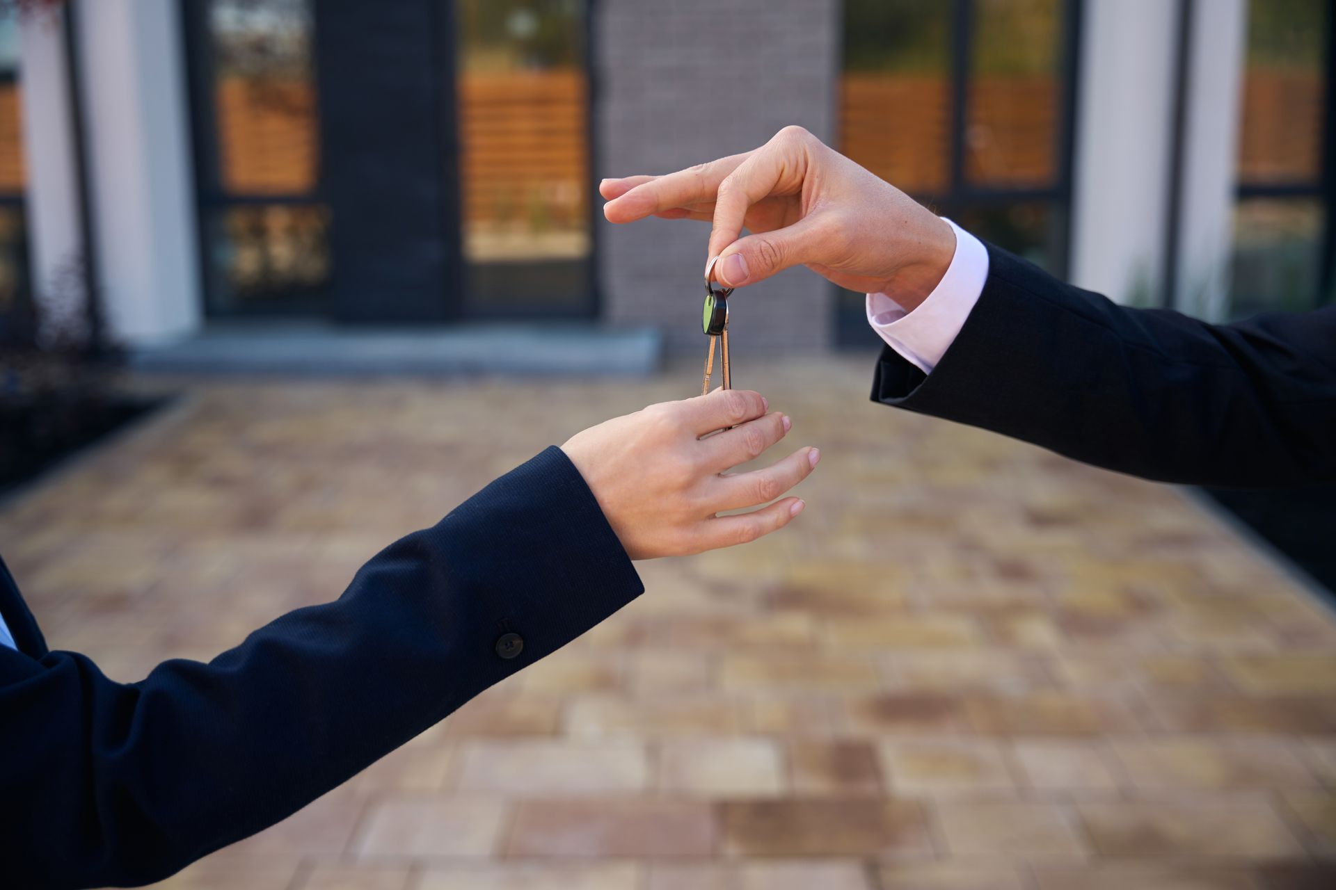 Hands exchanging keys in front of a house.