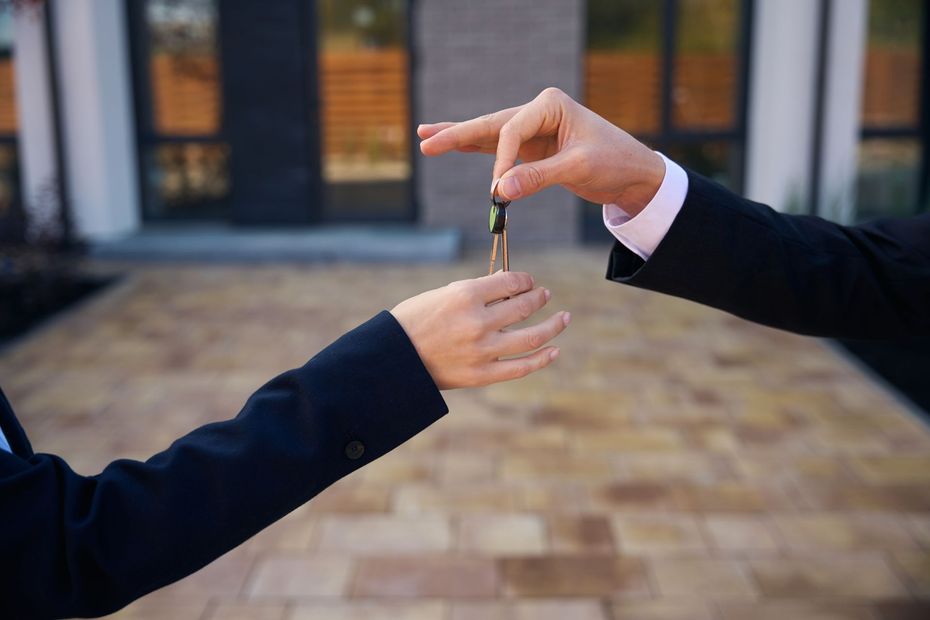 A man is handing a key to a woman in front of a house.
