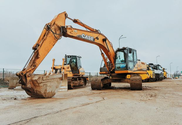 A row of construction vehicles are parked on a dirt road.
