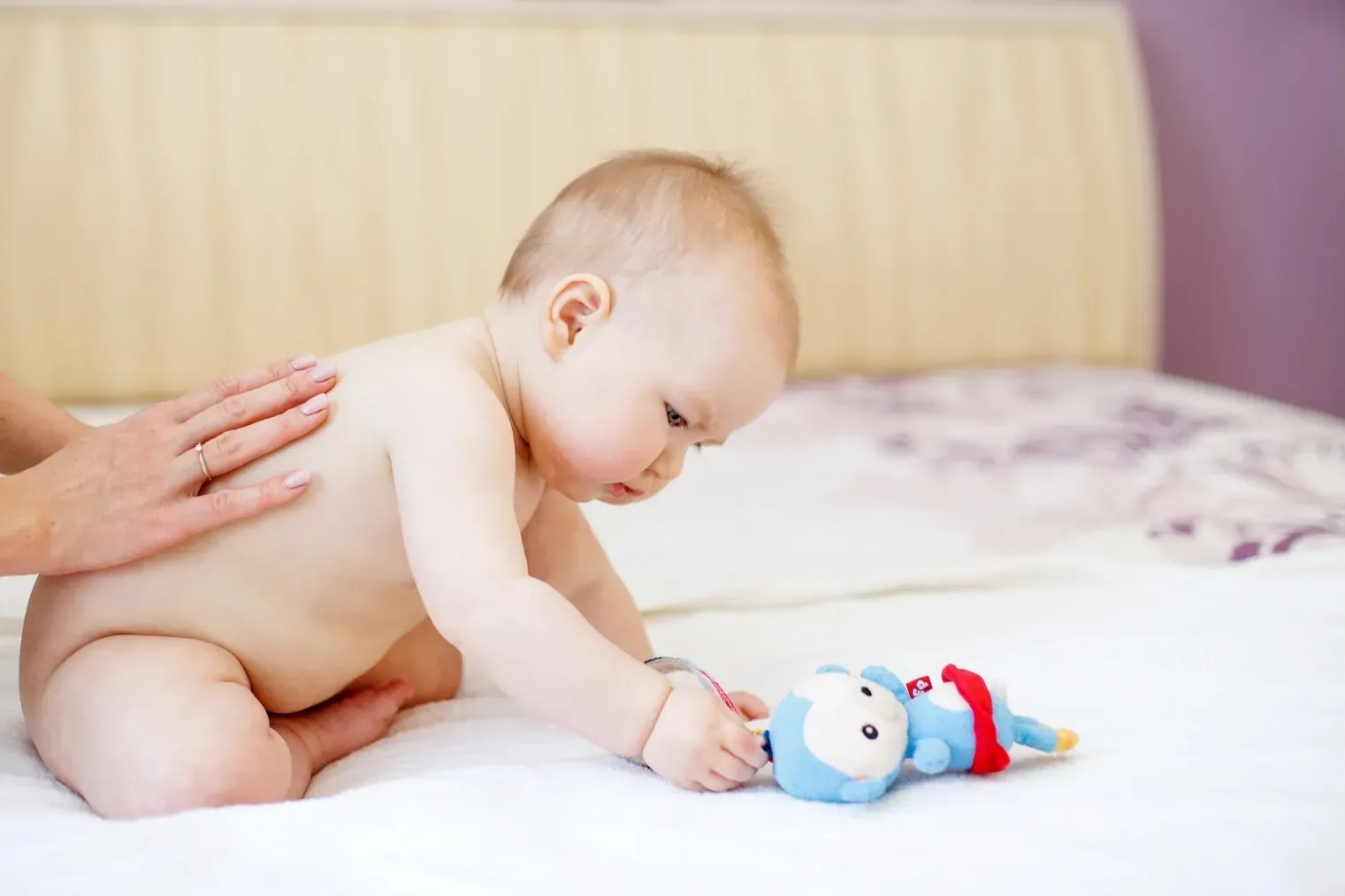 Un bébé joue avec un animal en peluche sur un lit.