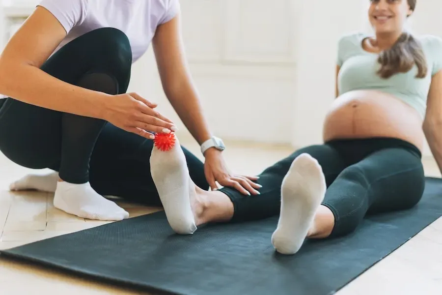 Une femme enceinte est assise sur un tapis de yoga et une femme est agenouillée à côté d'elle.