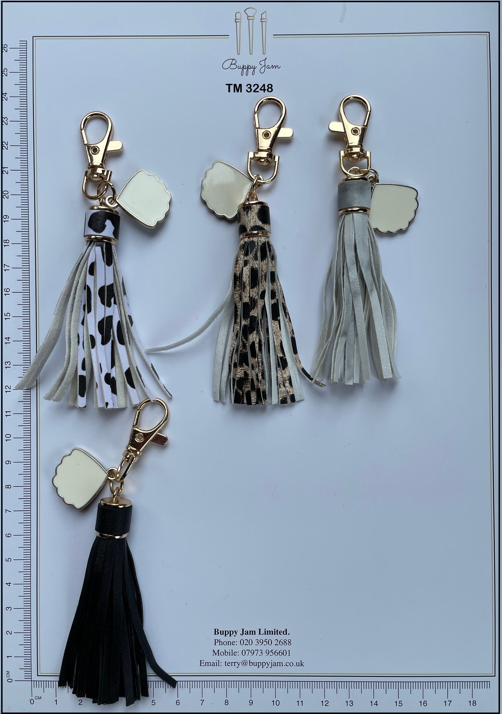 Three tassel keychains are displayed on a ruler