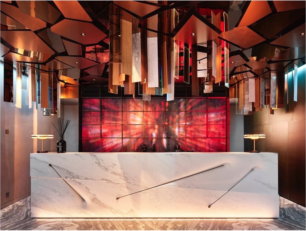 Hall dell'hotel con banchi per il check-in, pavimenti riflettenti, colonne decorate e un grande lampadario.