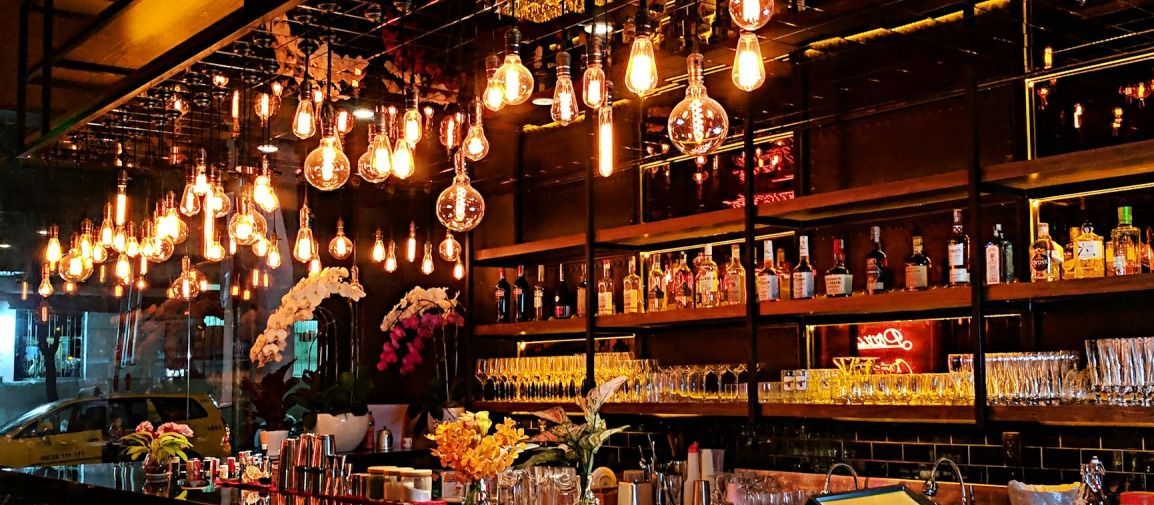 L'interno di un bar con luci sospese, scaffali pieni di liquori e bicchieri.