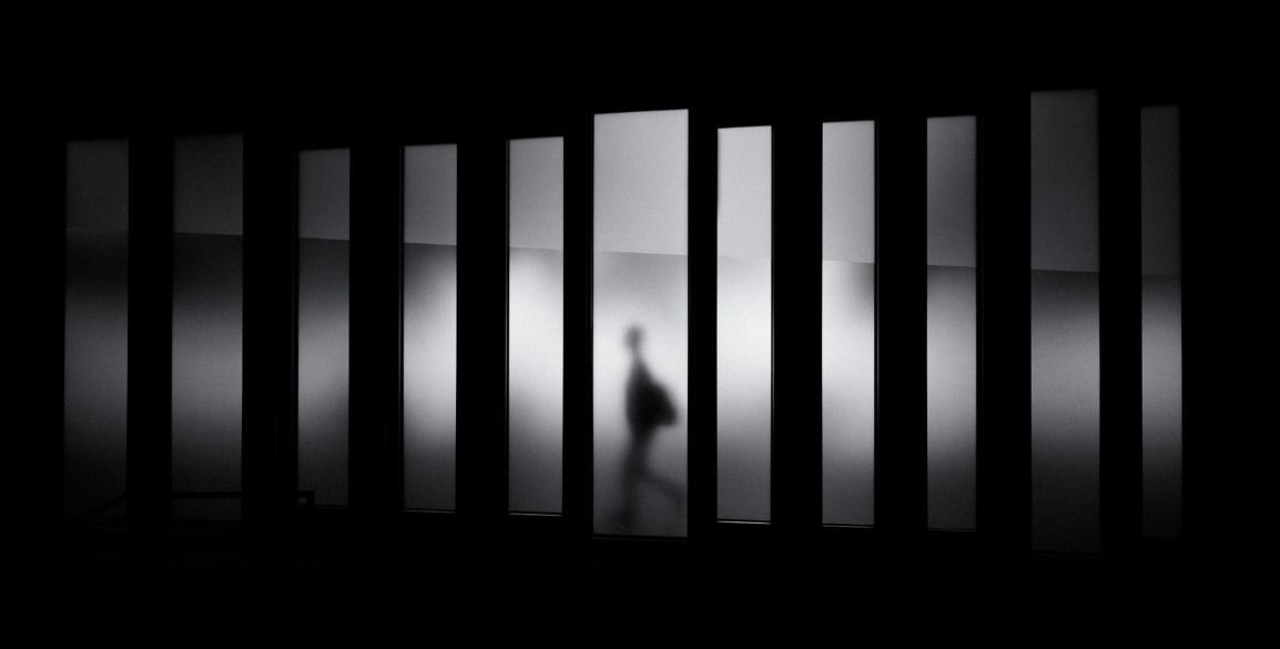 La sagoma di una persona che cammina tra pannelli verticali illuminati in uno spazio buio.