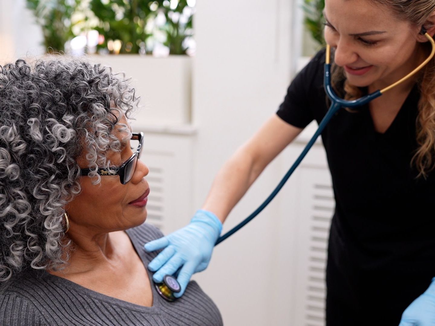 A nurse is listening to an older woman's heartbeat with a stethoscope