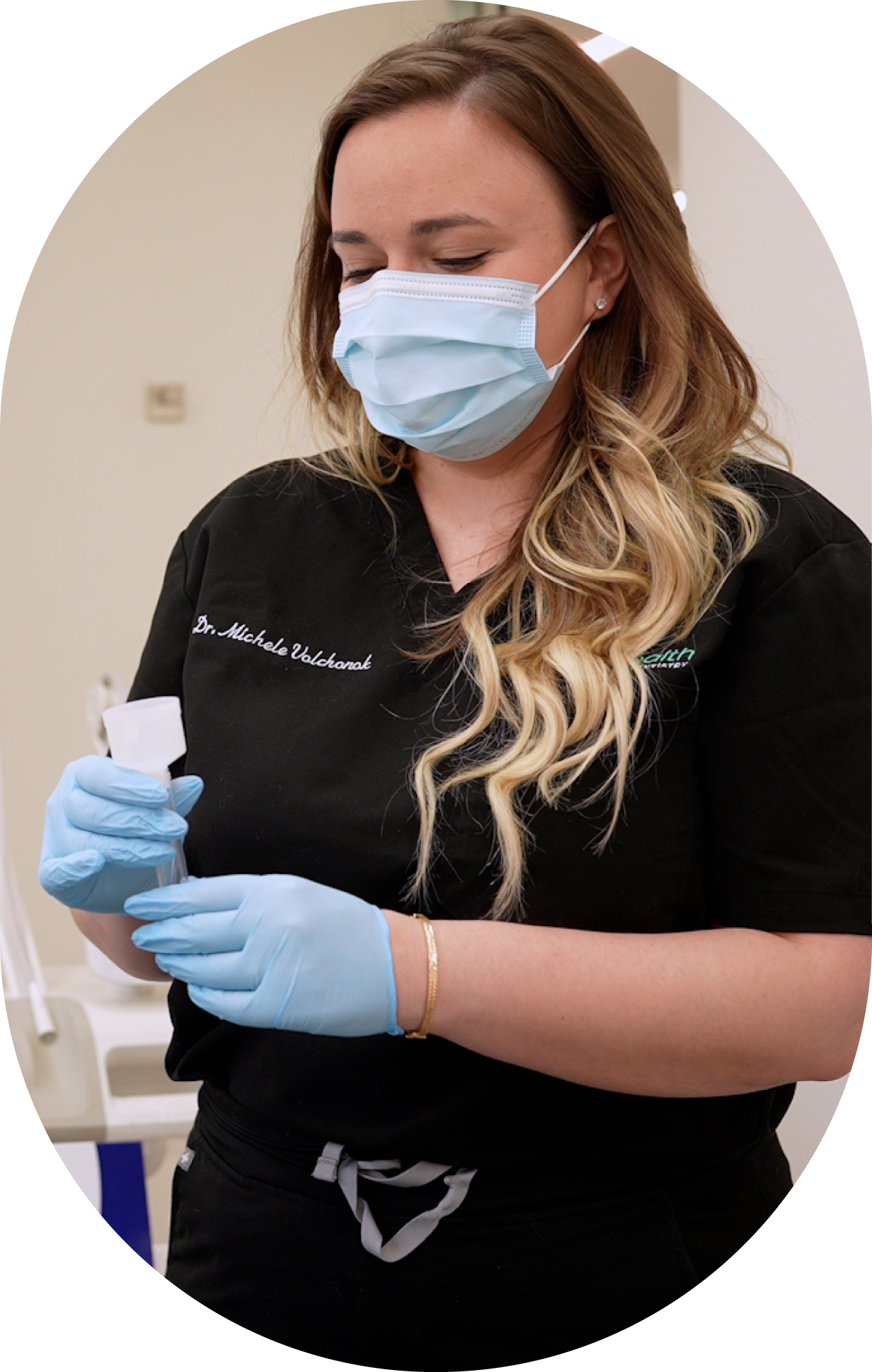 A woman wearing a mask and blue gloves is holding a dna collection cup