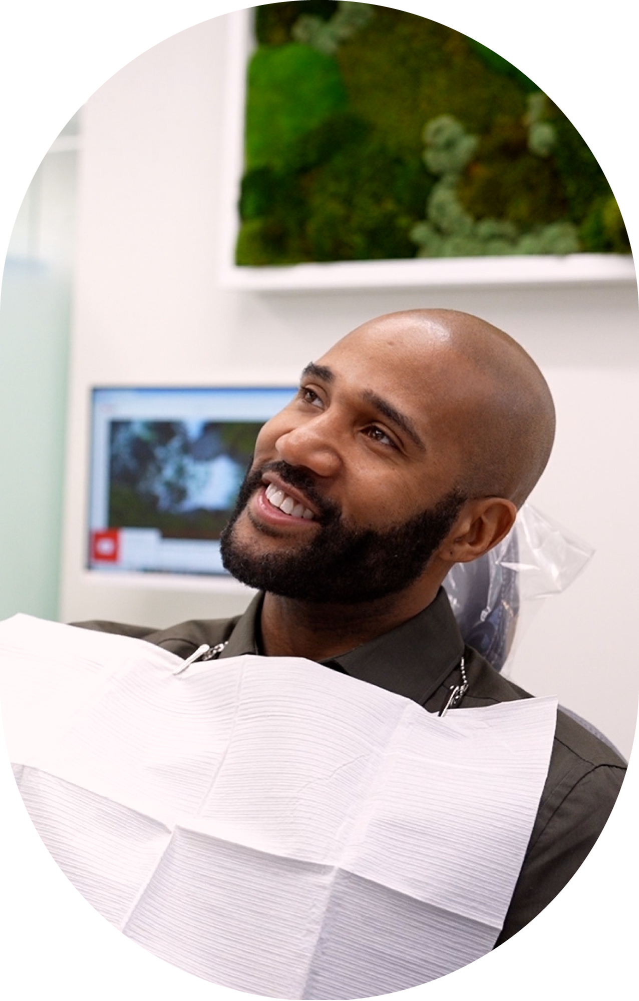 A man with a beard is smiling while sitting in a dental chair.