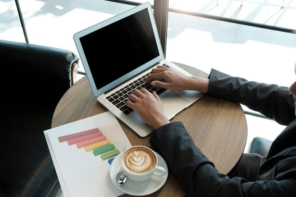 A Person Is Typing on A Laptop Computer While Sitting at A Table with A Cup of Coffee — Early Bird Accounts in Tamworth, NSW