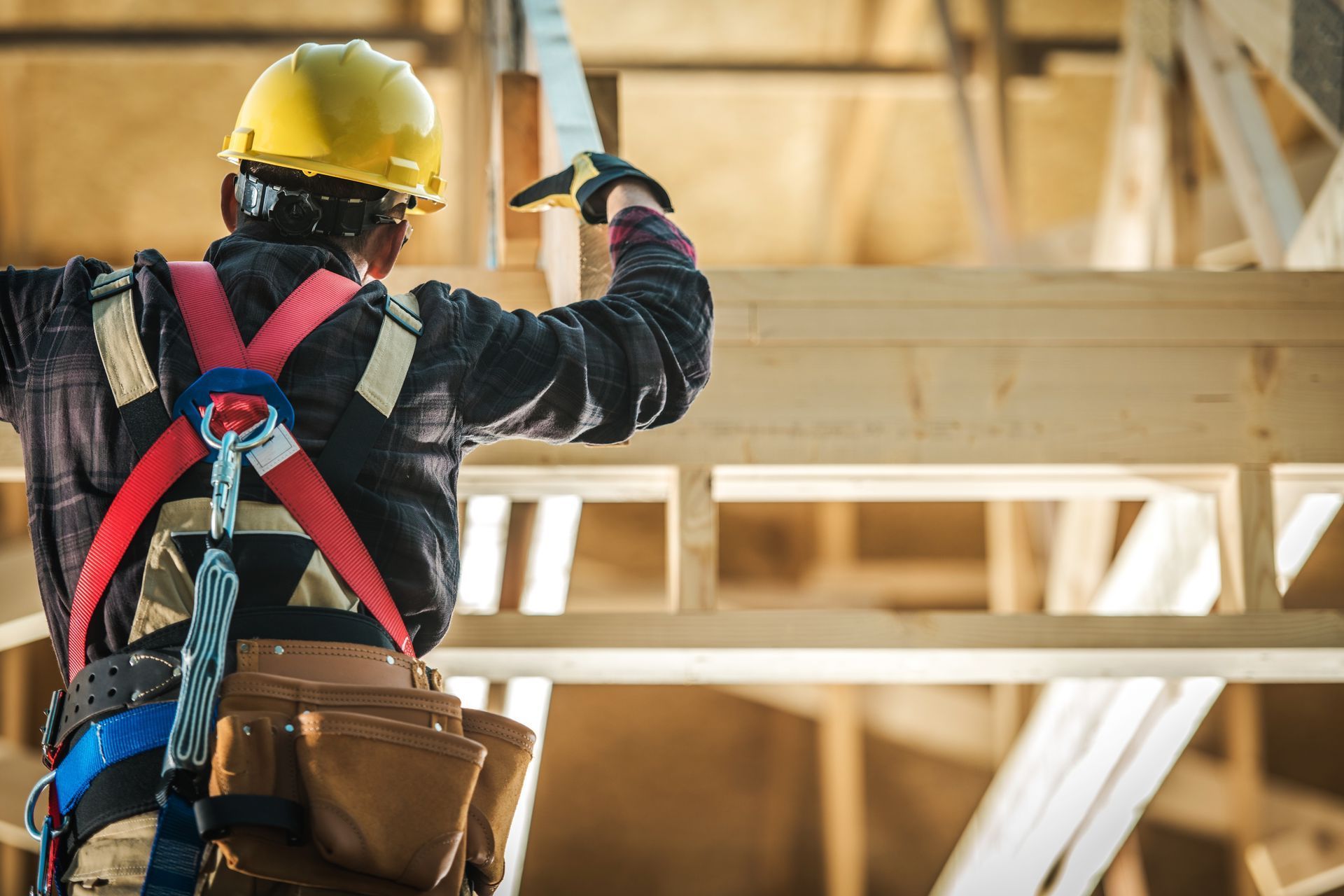 Un ouvrier du bâtiment portant un casque et un harnais de sécurité travaille sur une structure en bois.
