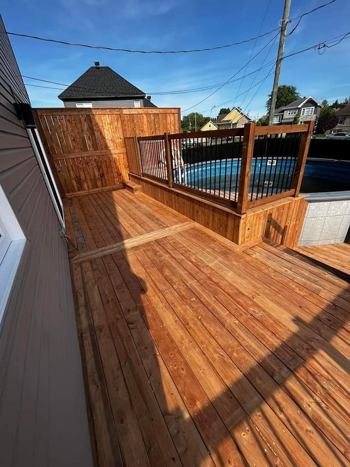 Une terrasse en bois avec une clôture et une piscine en arrière-plan.
