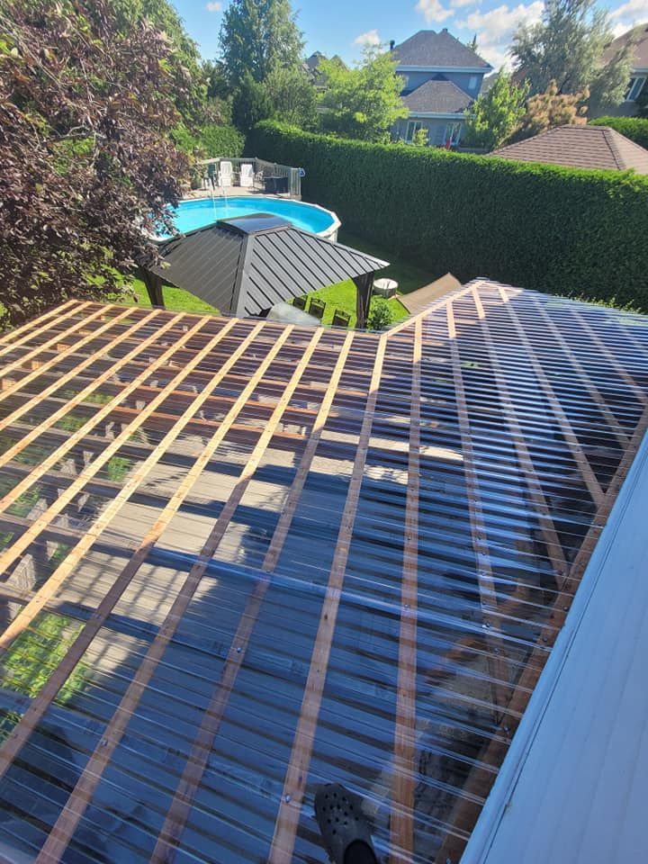 Un toit en plastique transparent est en cours d'installation sur une maison avec une piscine en arrière-plan.