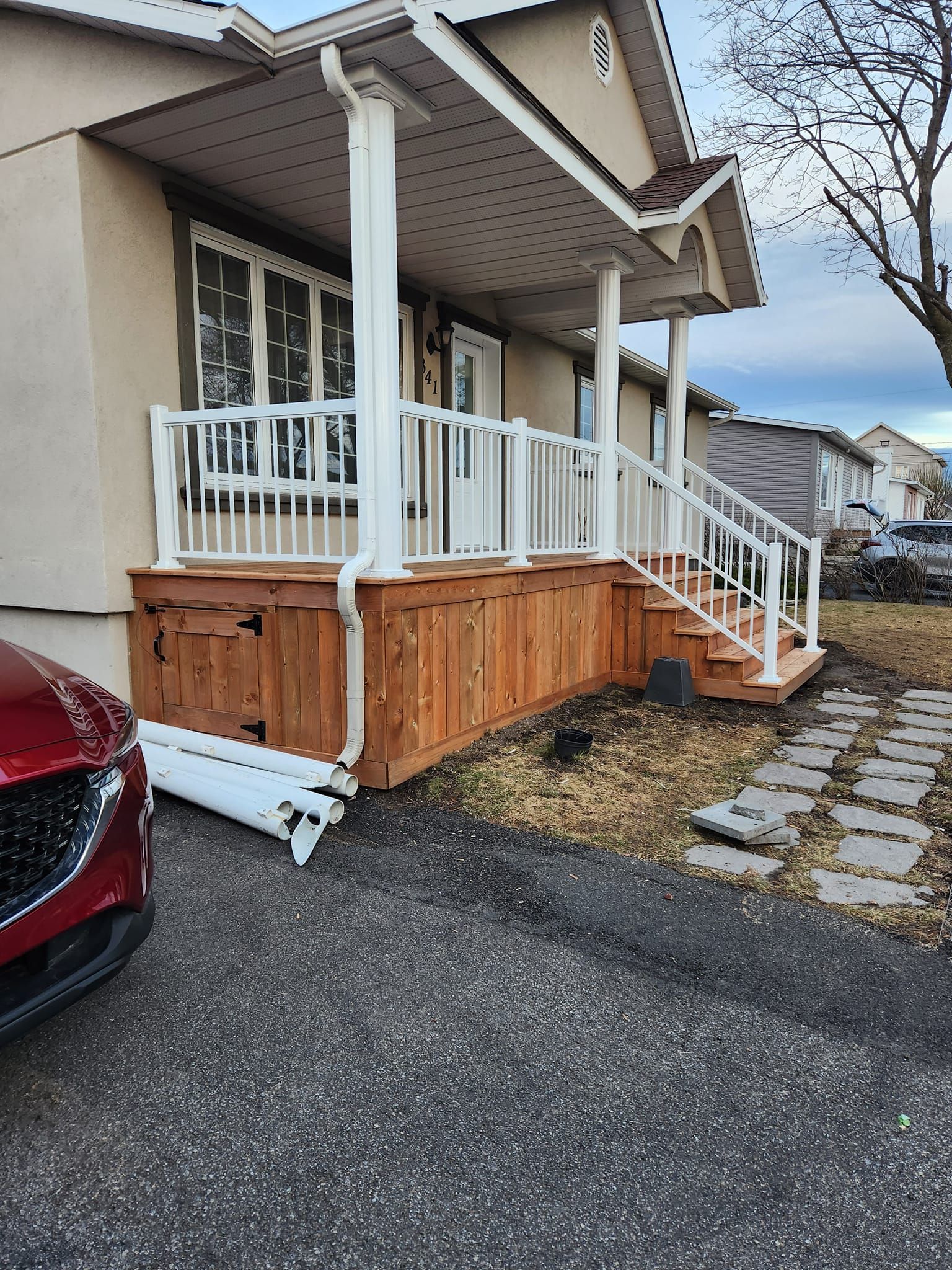 Une voiture rouge est garée devant une maison avec un porche et des escaliers.