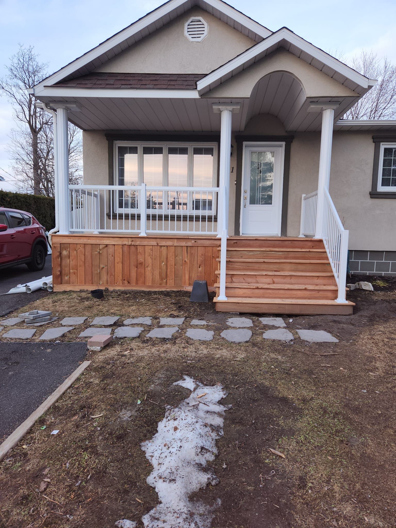 Une maison avec un porche et des escaliers et une voiture garée devant.