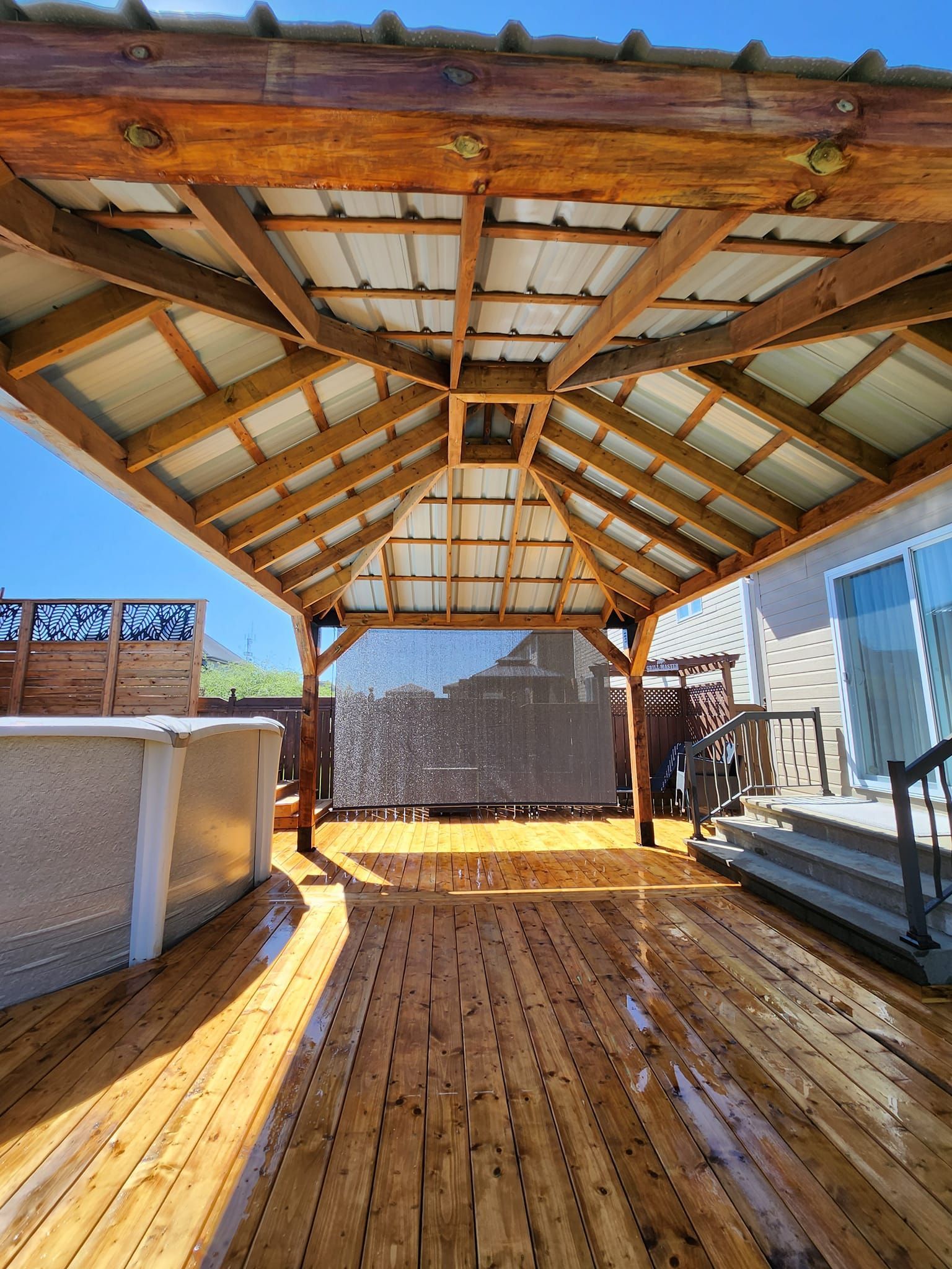 Une terrasse en bois avec un gazebo et un bain à remous en dessous.