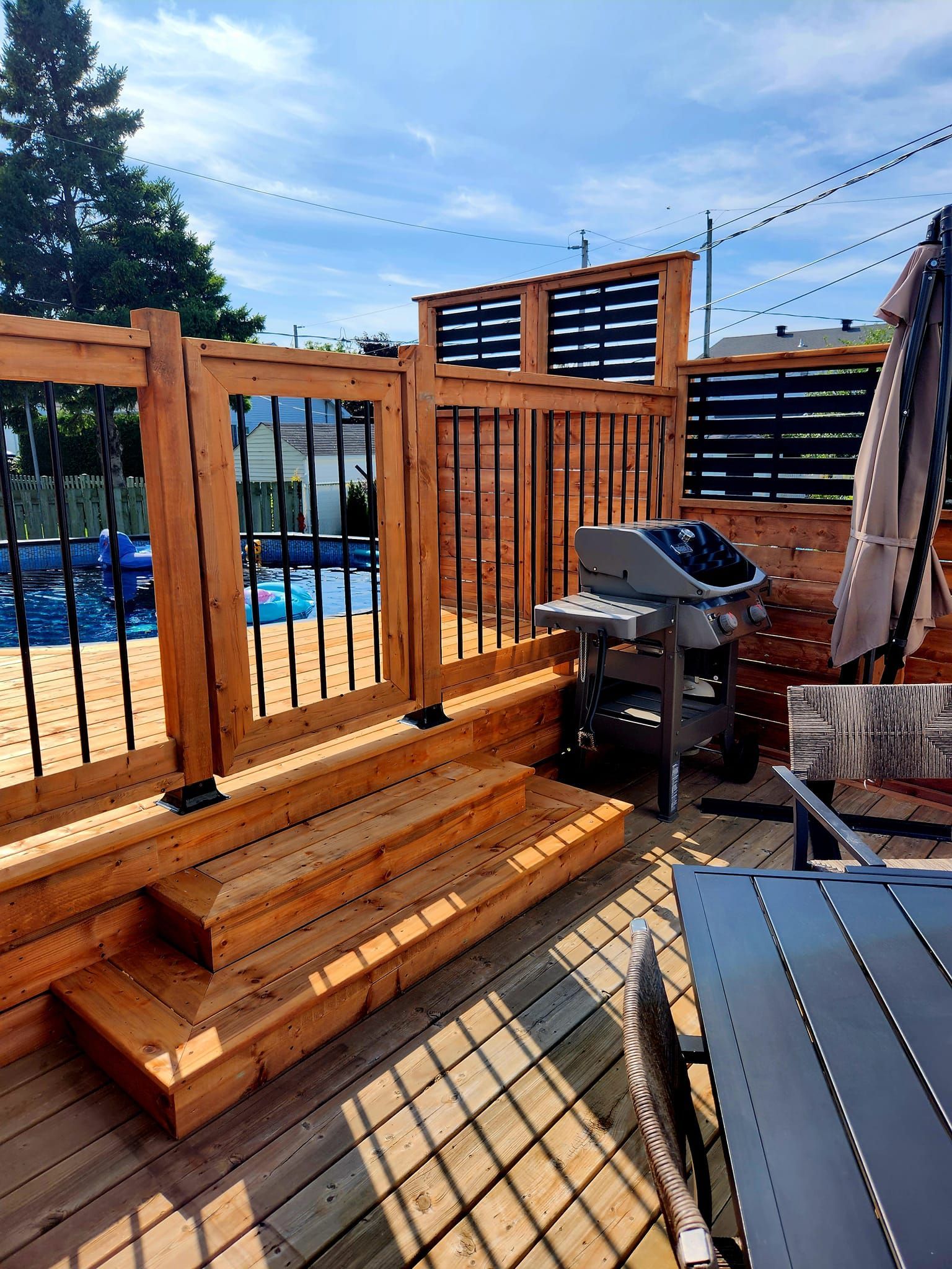 Une terrasse en bois avec un barbecue et des escaliers à côté d'une piscine.