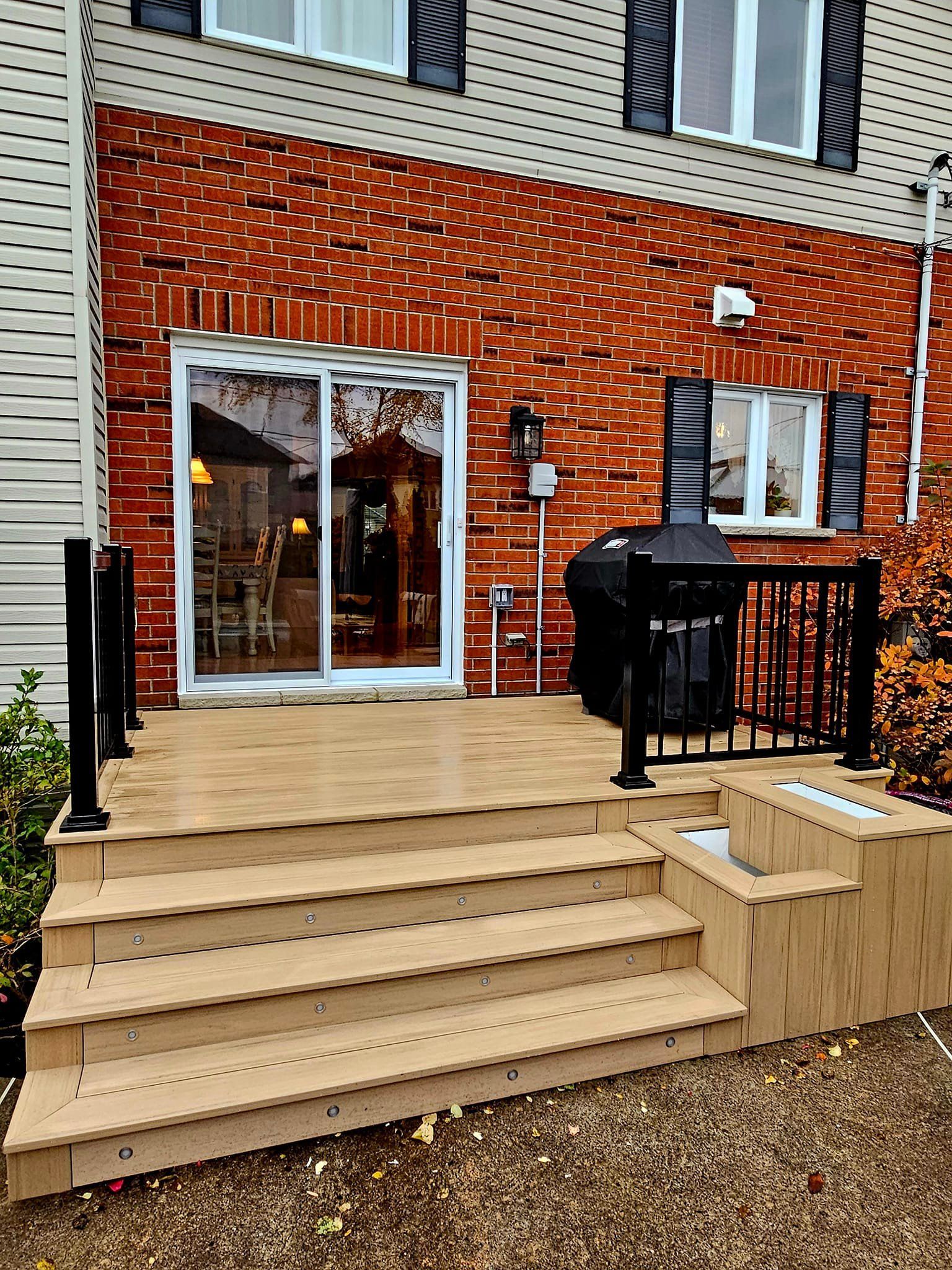 Une terrasse en bois avec des escaliers et un barbecue devant une maison en briques.