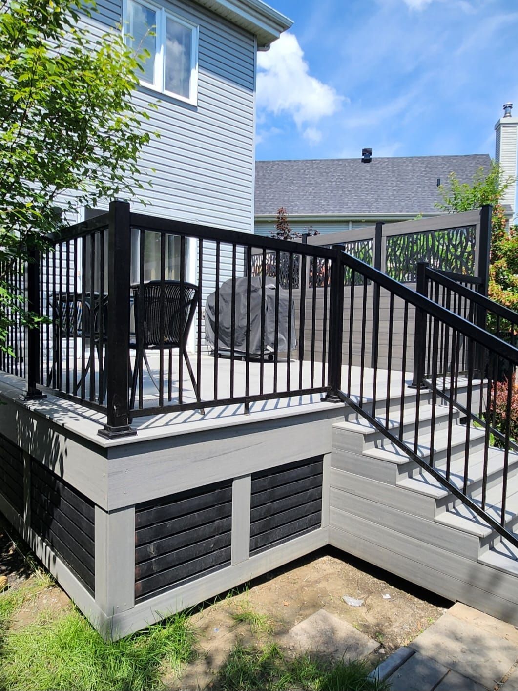 Une terrasse avec une balustrade noire et des escaliers devant une maison.