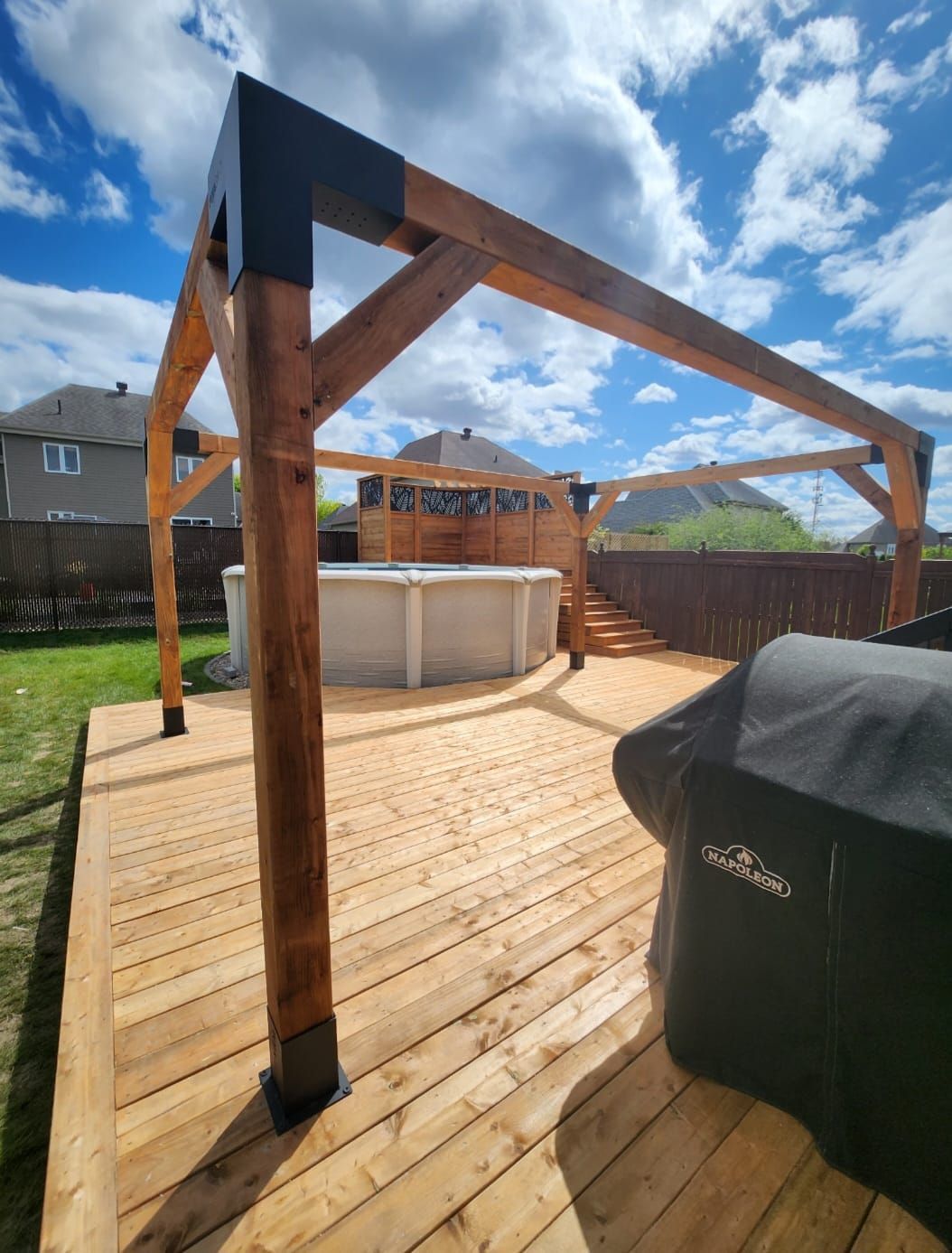 Une terrasse en bois avec un barbecue et une piscine en arrière-plan.