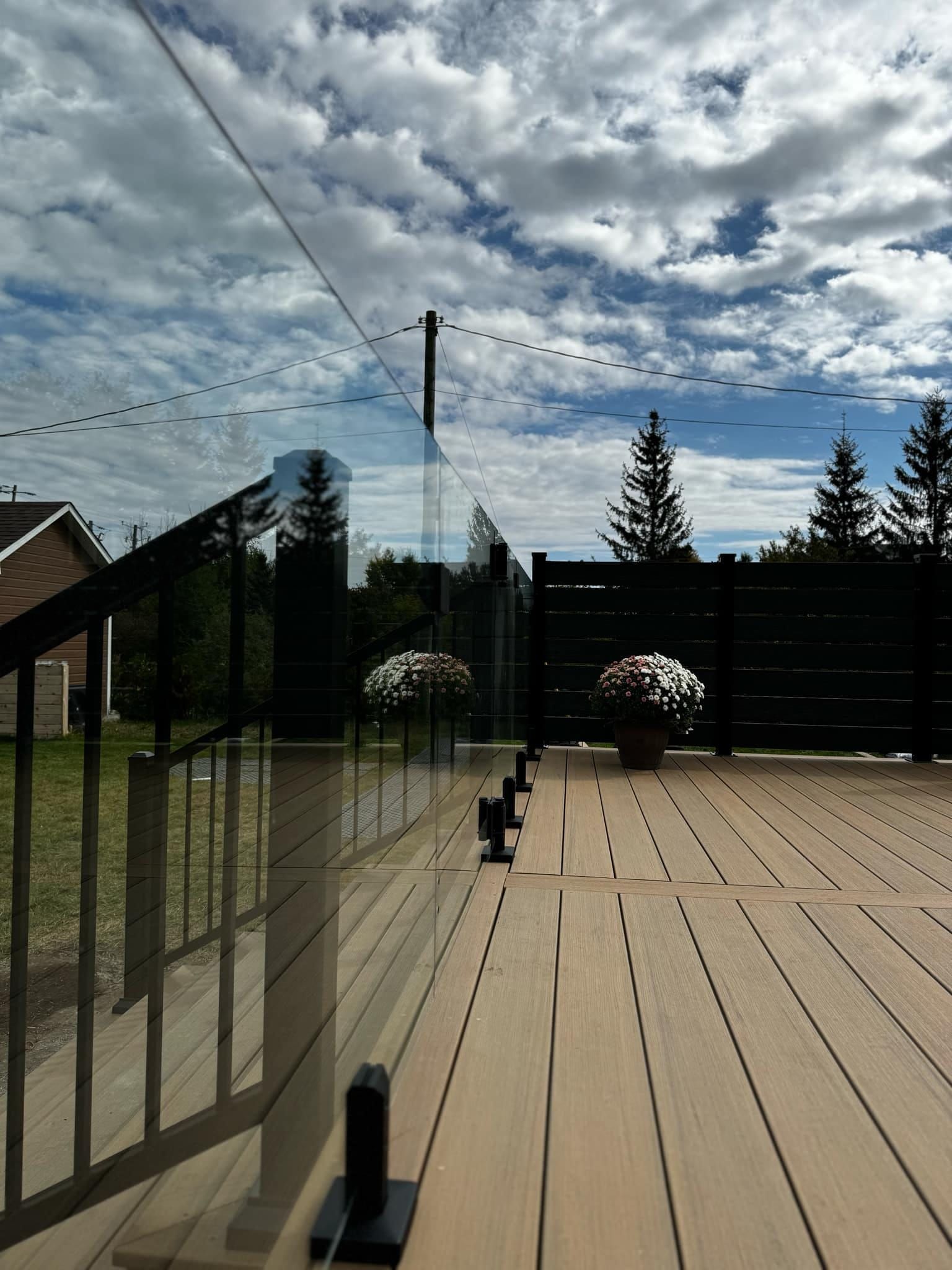 Une terrasse en bois avec une balustrade en verre et des fleurs dessus