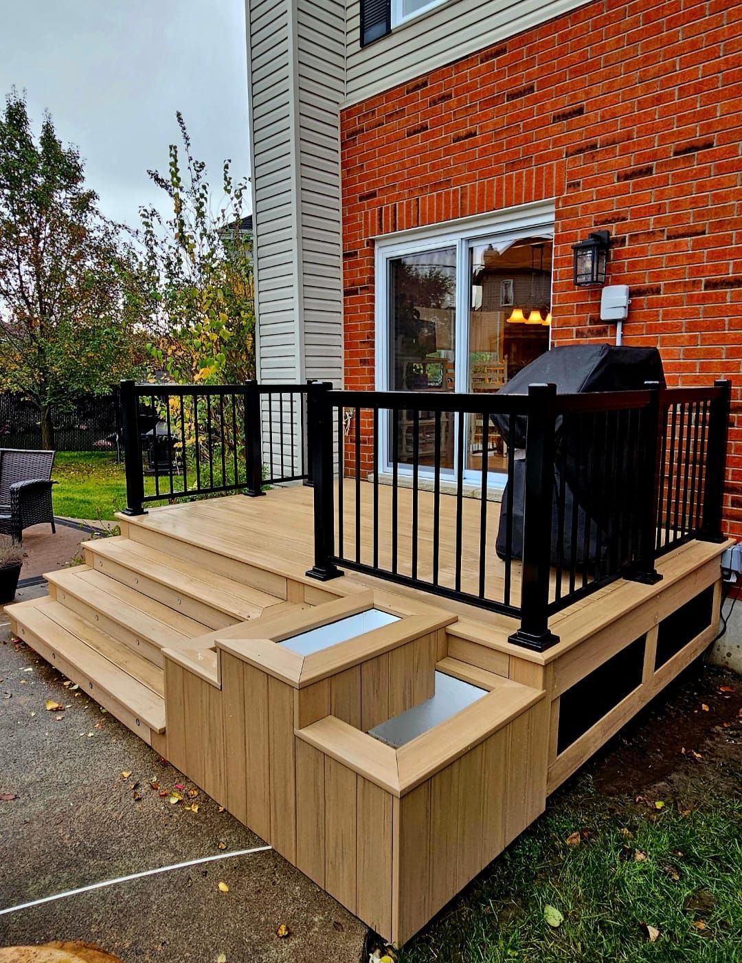 Une terrasse en bois avec des escaliers et un barbecue devant une maison en briques.