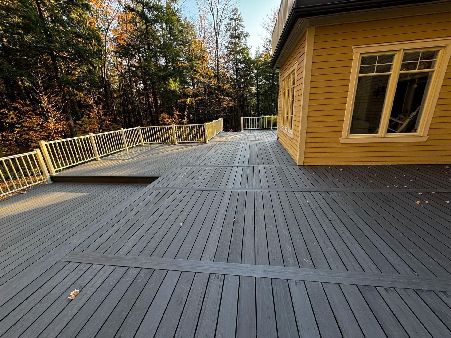 Une grande terrasse en bois avec une maison jaune en arrière-plan.