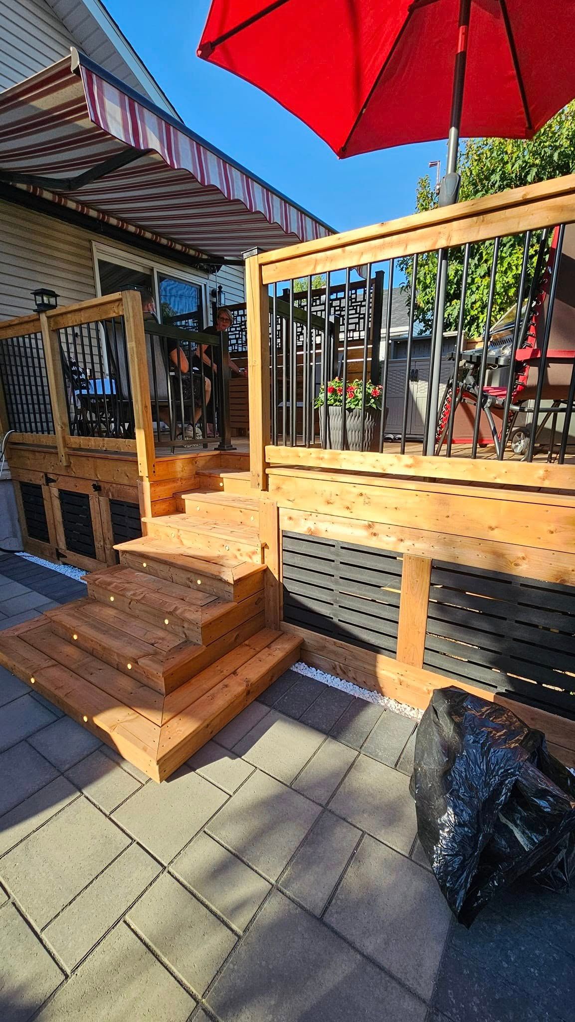 Une terrasse en bois avec des escaliers et un parasol rouge devant une maison.