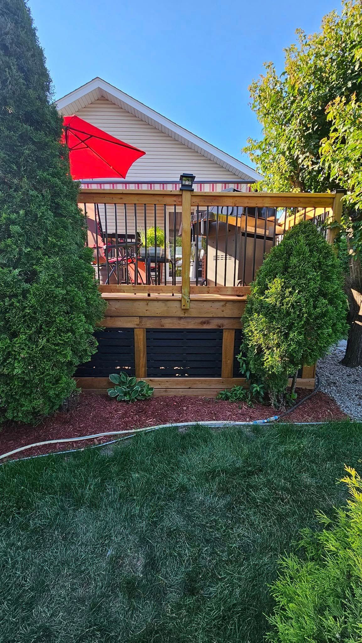 Une terrasse en bois avec un parasol rouge dans l'arrière-cour d'une maison.