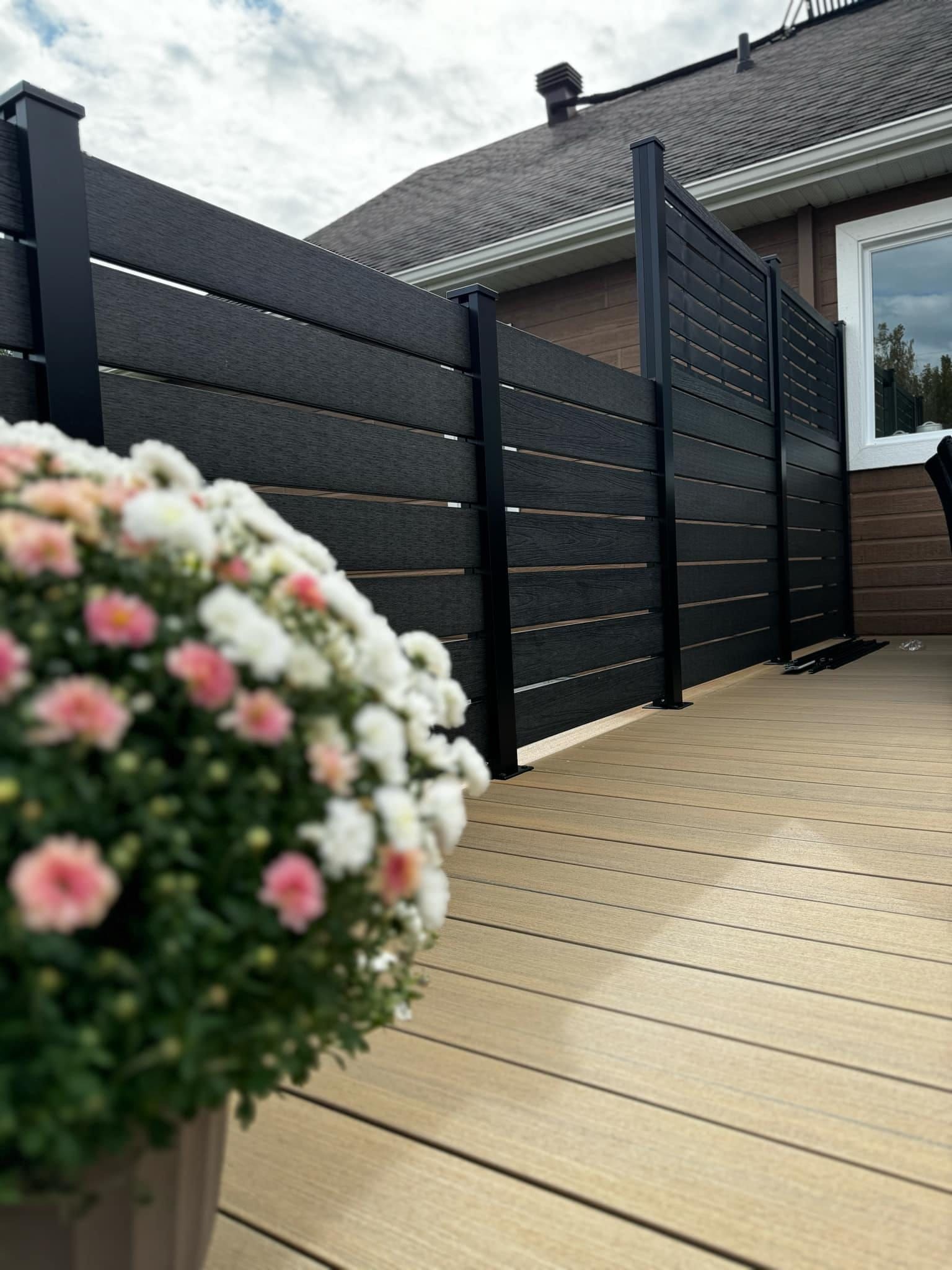 Une clôture noire entoure une terrasse avec des fleurs devant elle.