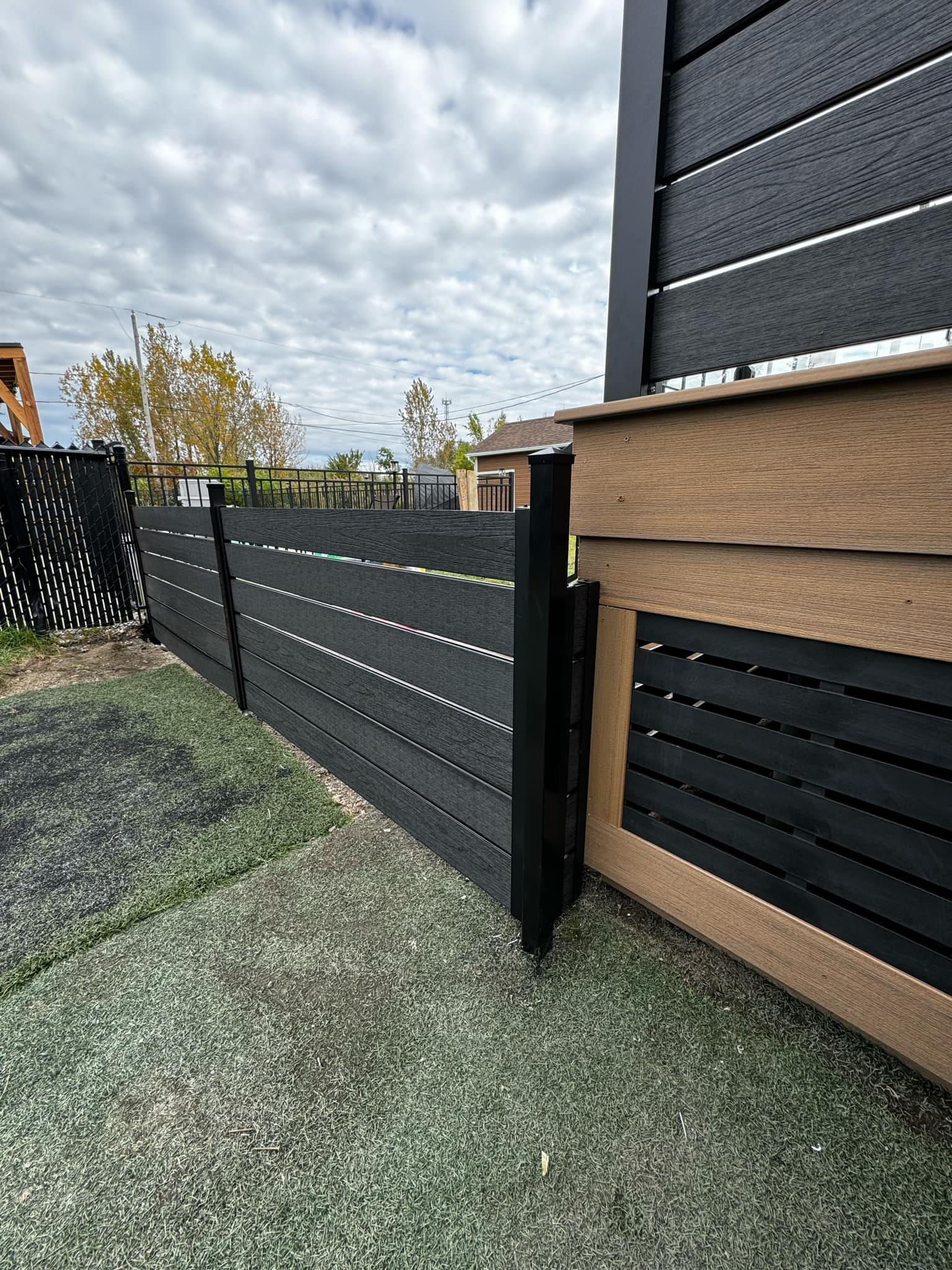 Une clôture en bois noir entoure une maison dans une arrière-cour.